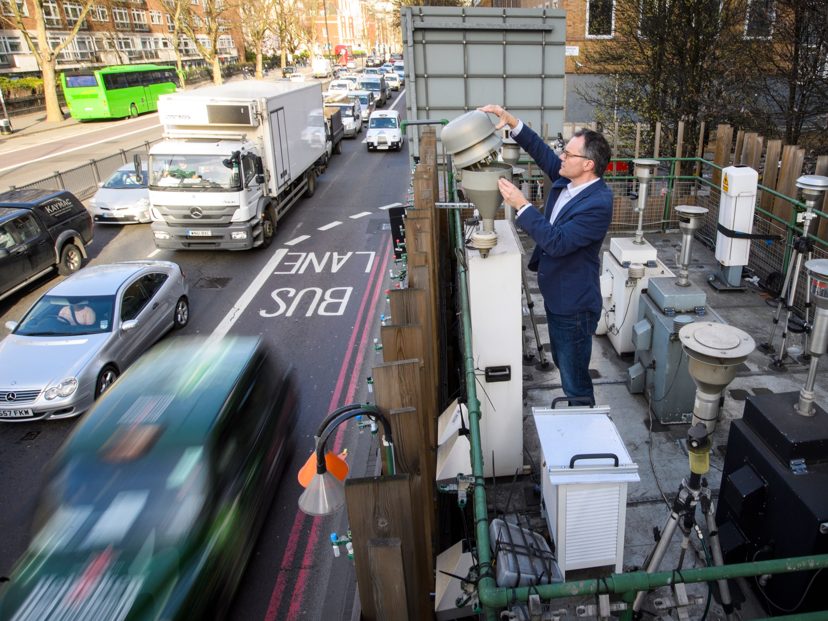 a person lifting the top of a funnel-shaped container on a patio just above a busy road